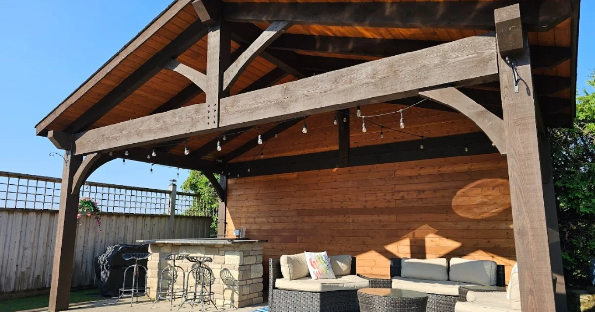 Timber frame pavilion beside a swimming pool with lounge chairs, a sectional sofa, and vibrant blue cushions.